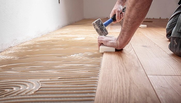 Un artisan travaille sur la pose de parquet en chêne dans une maison, rénovant le sol pour un résultat élégant et durable. La rénovation inclut la préparation du sol et l'installation méticuleuse des planches de parquet