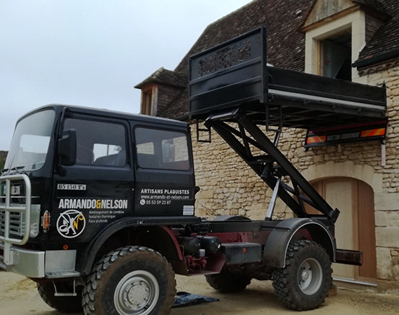 Un camion est stationné à côté d'une maison, chargé de matériaux d'isolation intérieure. Des ouvriers s'affairent à décharger les panneaux isolants en polystyrène ou en laine minérale, prêts à être installés à l'intérieur de la maison pour améliorer l'efficacité énergétique et le confort thermique. Le camion, équipé de logos et d'informations sur les services d'isolation, démontre l'engagement de l'entreprise à fournir des solutions d'isolation de haute qualité. La scène met en évidence l'importance de la préparation et du transport sécurisé des matériaux pour des projets d'isolation réussis.