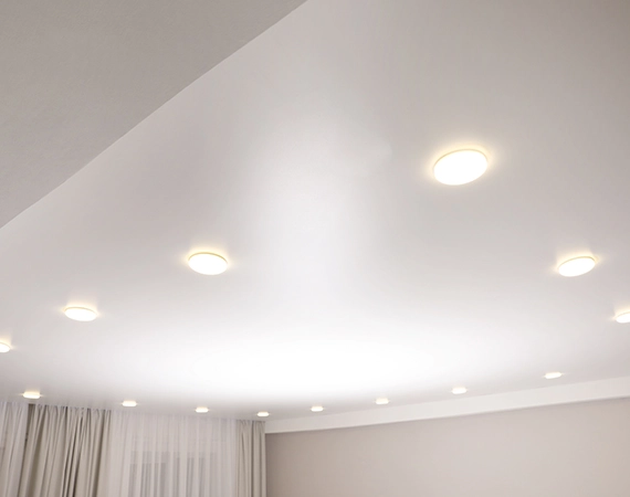 Des spots lumineux sont installés dans un faux plafond en toile tendue. Les lumières encastrées créent une ambiance moderne et élégante